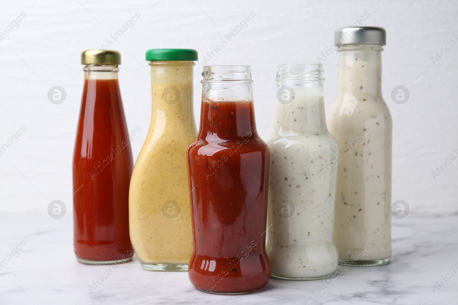 Photo of Tasty sauces in glass bottles on white marble table, closeup