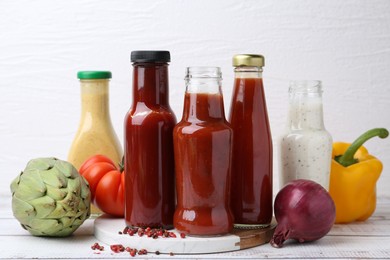 Photo of Tasty sauces in glass bottles and fresh products on white wooden table, closeup