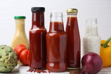 Photo of Tasty sauces in glass bottles and fresh products on white wooden table, closeup