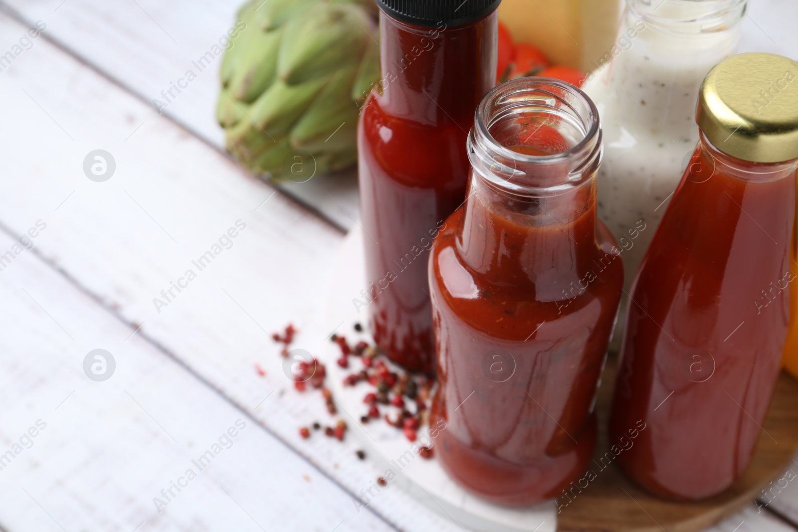 Photo of Tasty sauces in glass bottles and fresh products on white wooden table, closeup. Space for text