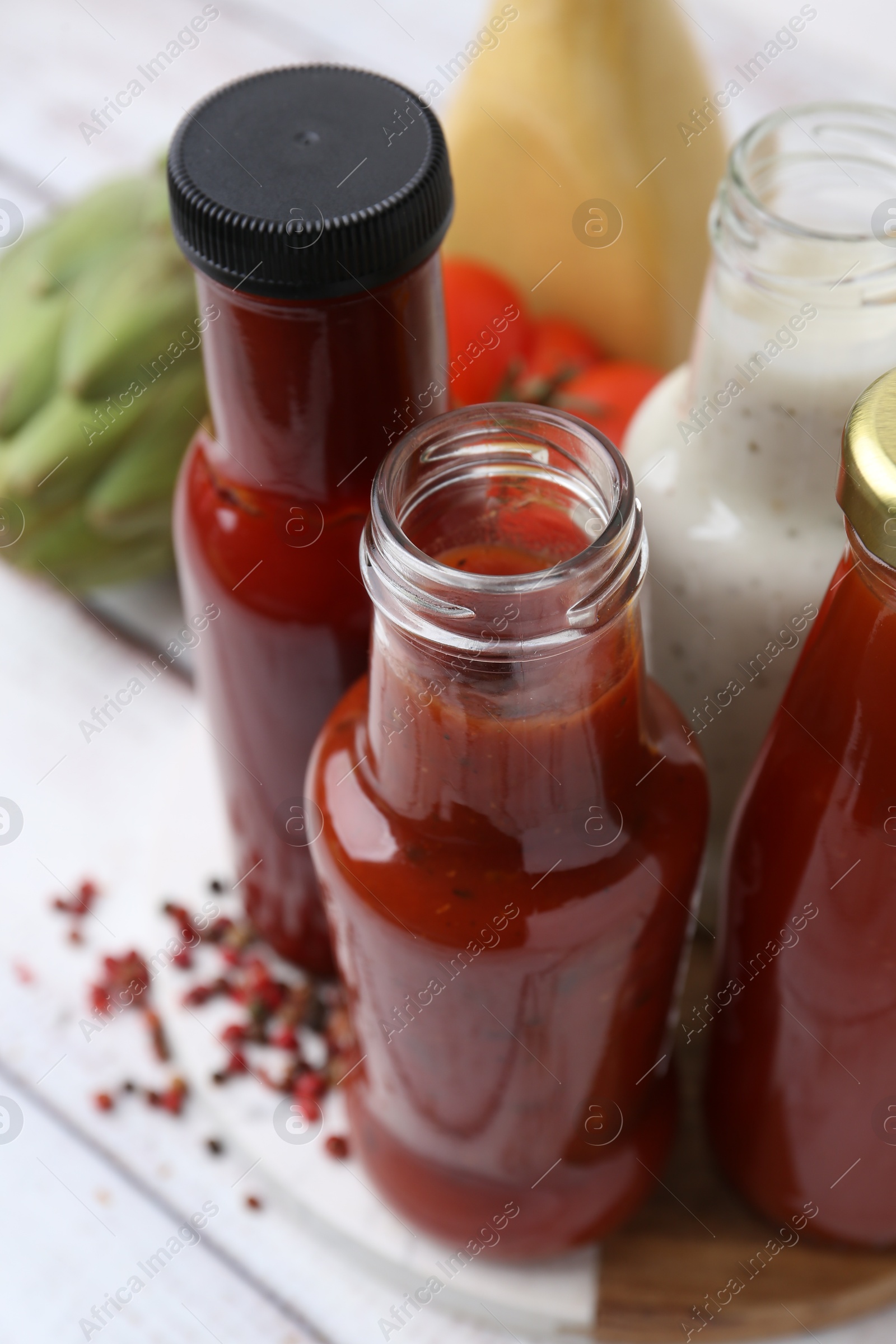 Photo of Tasty sauces in glass bottles and fresh products on white wooden table, closeup