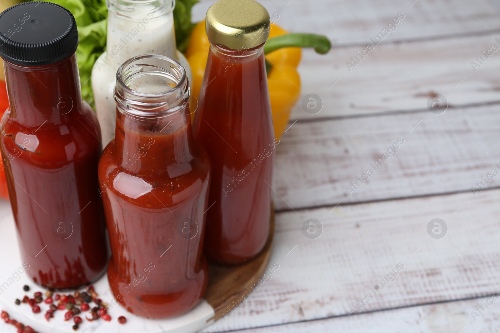 Photo of Tasty sauces in glass bottles and fresh products on white wooden table, closeup. Space for text