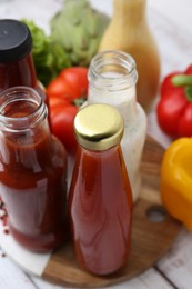 Photo of Tasty sauces in glass bottles and fresh products on white wooden table, closeup