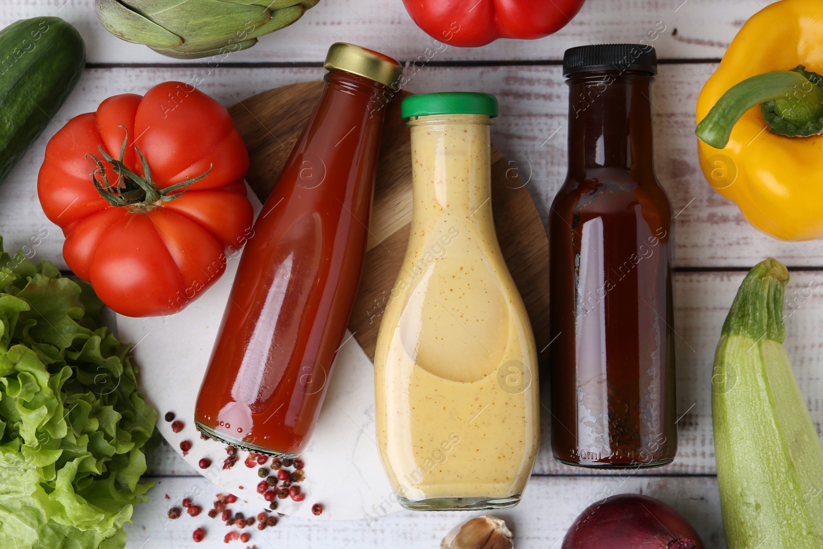 Photo of Tasty sauces in glass bottles and fresh products on white wooden table, flat lay