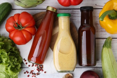 Tasty sauces in glass bottles and fresh products on white wooden table, flat lay