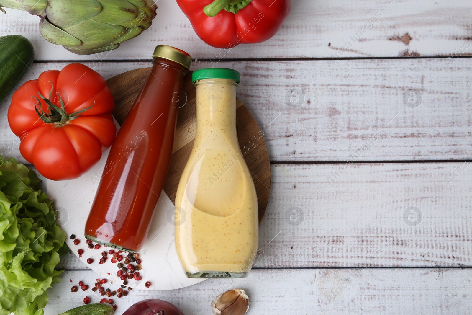 Photo of Tasty sauces in glass bottles and fresh products on white wooden table, flat lay. Space for text