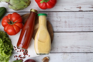 Photo of Tasty sauces in glass bottles and fresh products on white wooden table, flat lay. Space for text