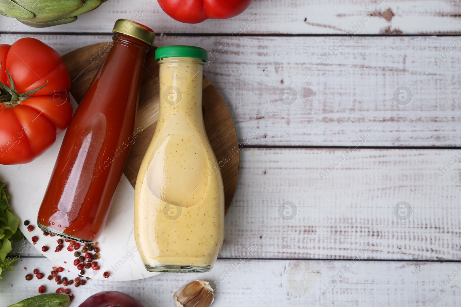 Photo of Tasty sauces in glass bottles and fresh products on white wooden table, flat lay. Space for text