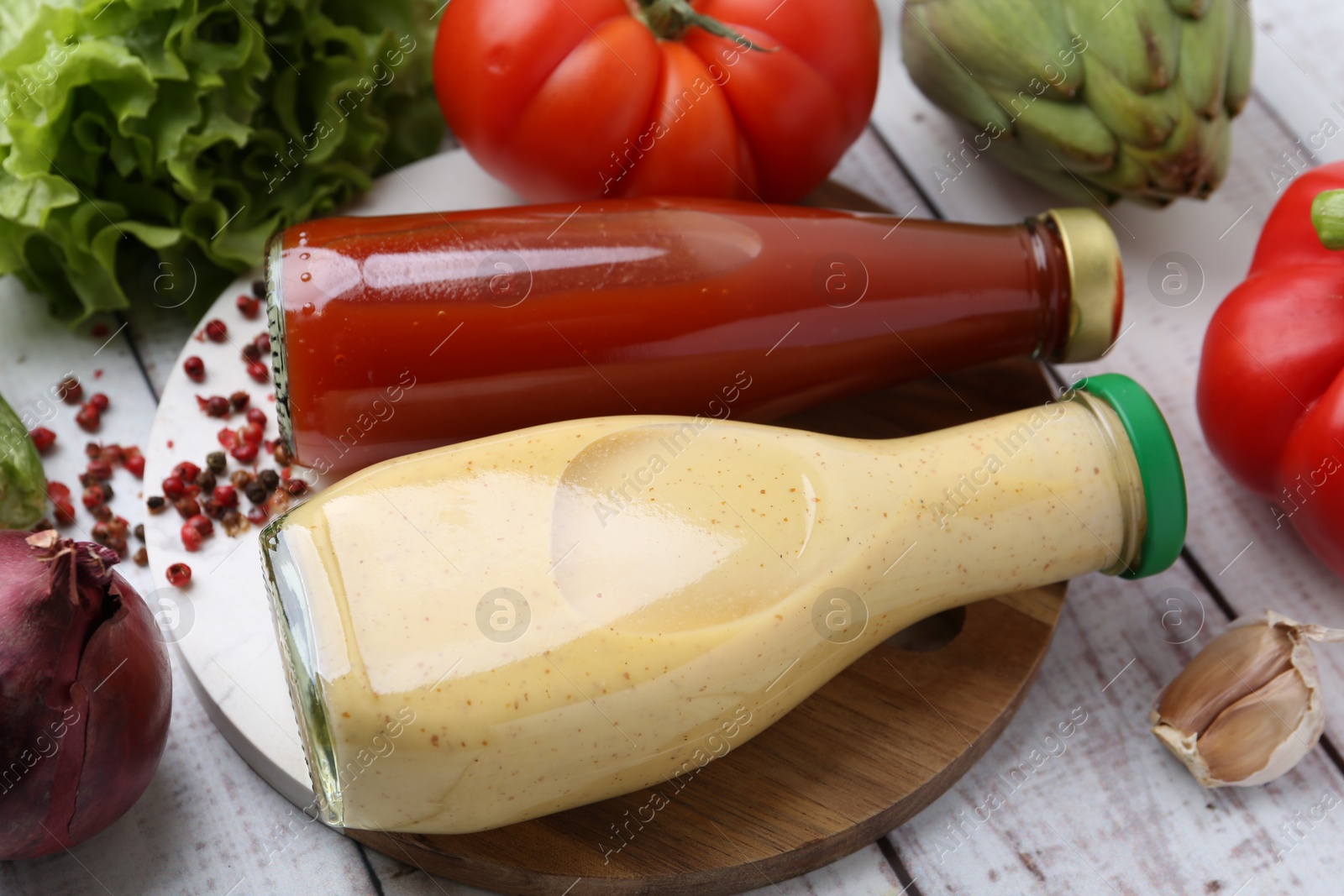 Photo of Tasty sauces in glass bottles and fresh products on white wooden table, closeup