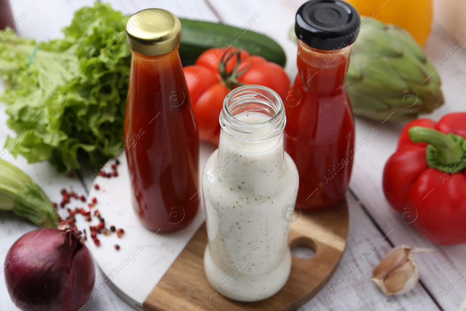 Photo of Tasty sauces in glass bottles and fresh products on white wooden table, closeup