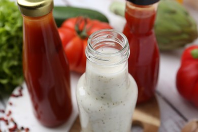 Photo of Tasty sauces in glass bottles and fresh products on white wooden table, closeup