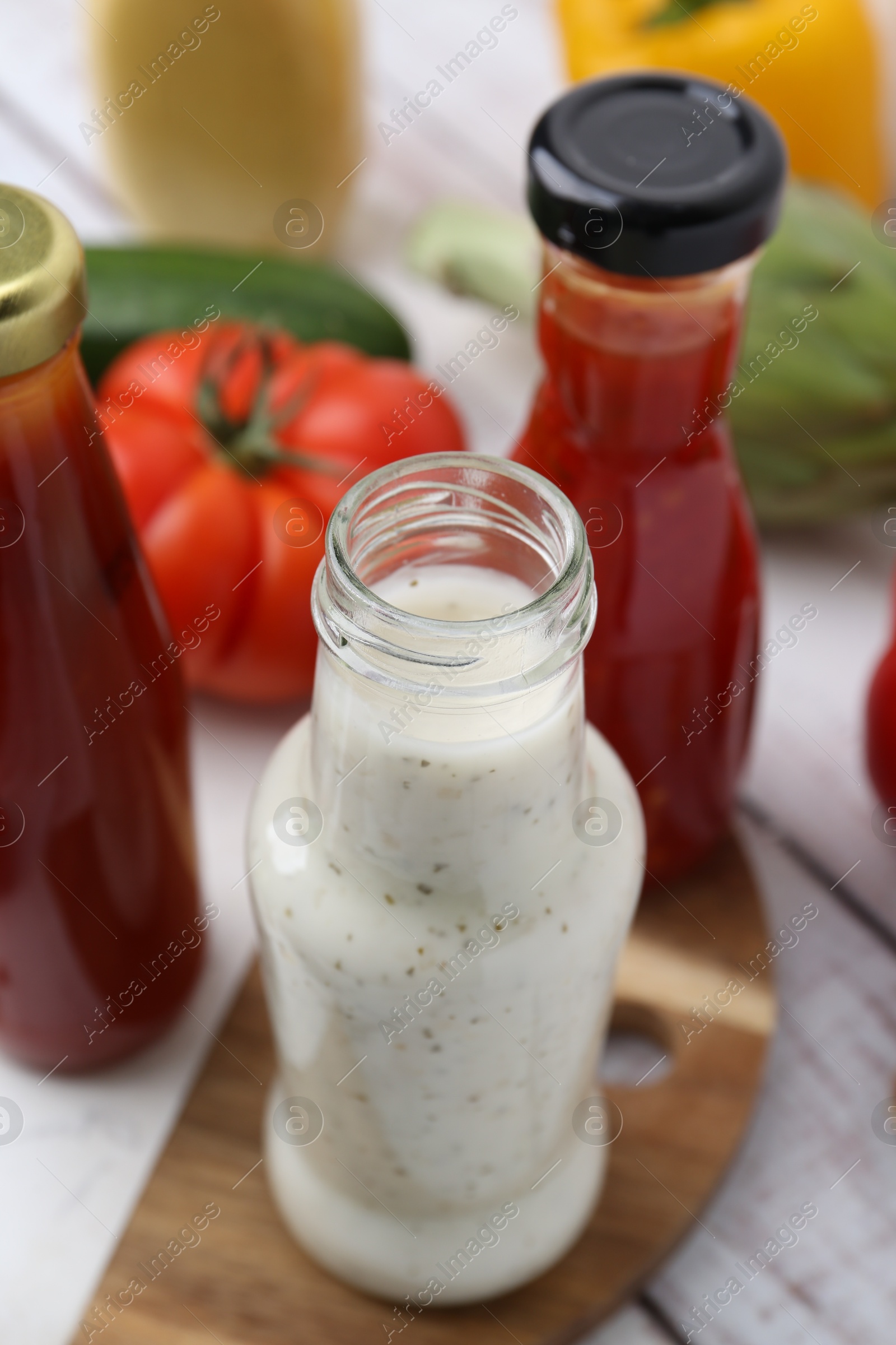 Photo of Tasty sauces in glass bottles and fresh products on white wooden table, closeup