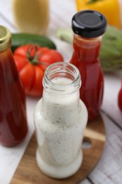 Photo of Tasty sauces in glass bottles and fresh products on white wooden table, closeup