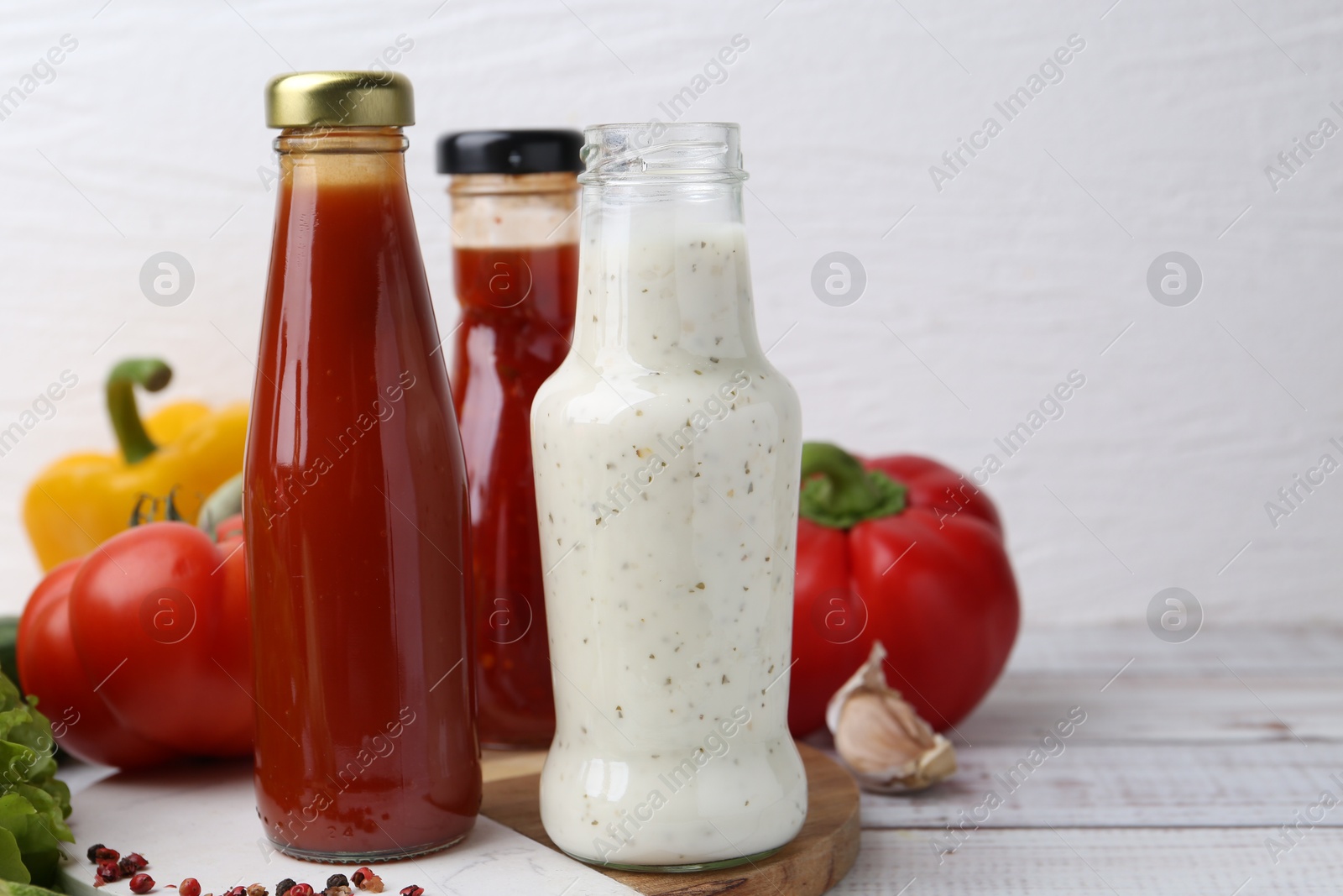 Photo of Tasty sauces in glass bottles and fresh products on white wooden table, closeup. Space for text