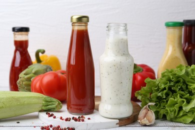 Photo of Tasty sauces in glass bottles and fresh products on white wooden table, closeup