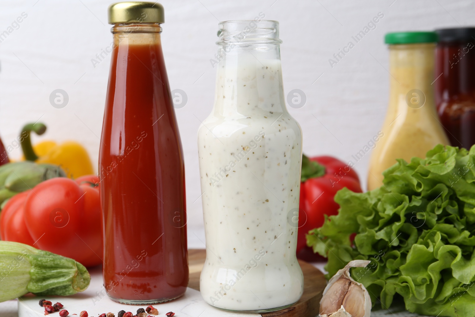 Photo of Tasty sauces in glass bottles and fresh products on white wooden table, closeup