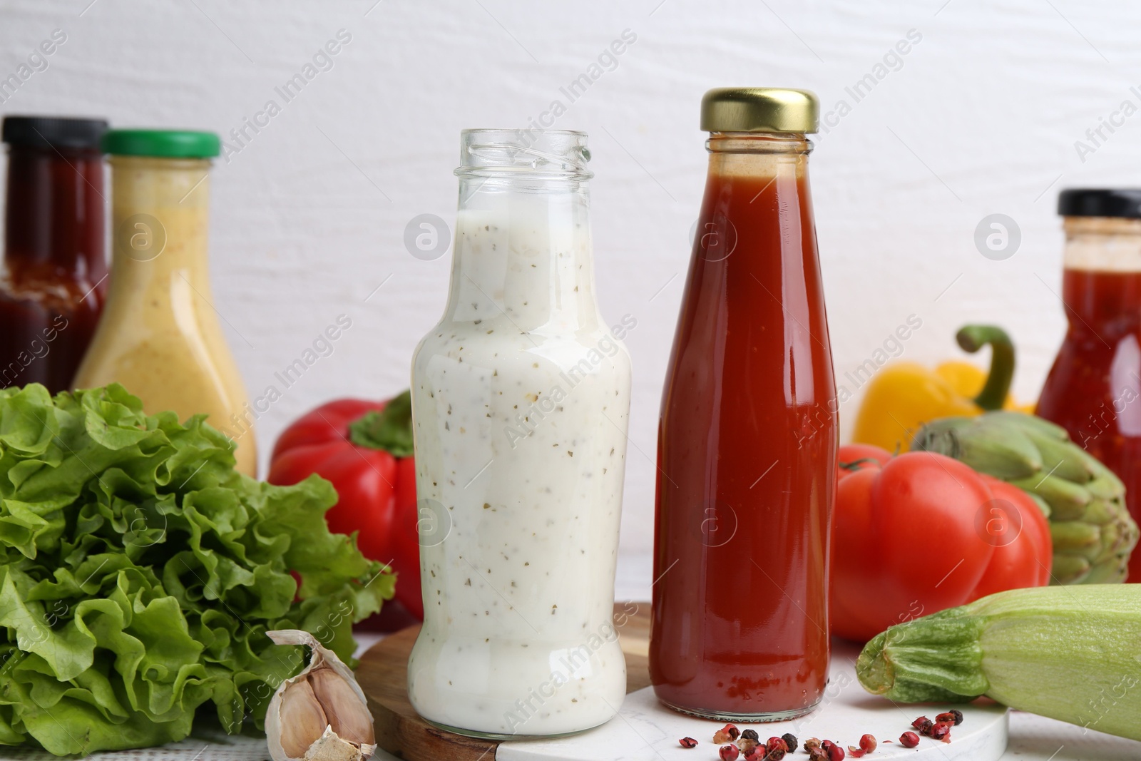 Photo of Tasty sauces in glass bottles and fresh products on white wooden table, closeup