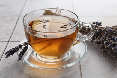 Photo of Aromatic lavender tea in glass cup and dry flowers on white tiled table, closeup