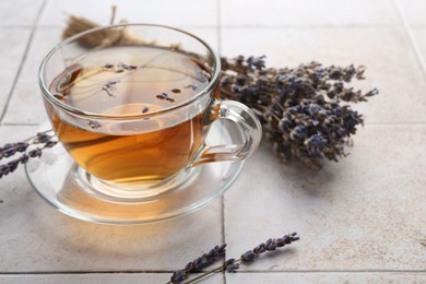 Photo of Aromatic lavender tea in glass cup and dry flowers on white tiled table, closeup