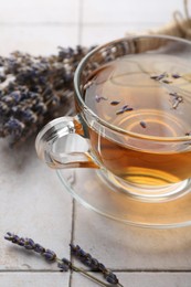 Aromatic lavender tea in glass cup and dry flowers on white tiled table, closeup