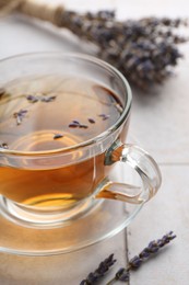 Photo of Aromatic lavender tea in glass cup and dry flowers on white tiled table, closeup