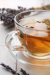 Aromatic lavender tea in glass cup and dry flowers on white tiled table, closeup