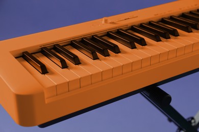 Image of Orange synthesizer on violet background, closeup. Electronic musical instrument