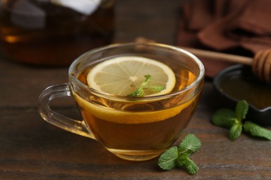 Photo of Tasty mint tea in cup, lemon and fresh leaves on wooden table, closeup