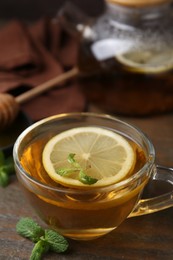 Photo of Tasty mint tea in cup, lemon and fresh leaves on wooden table, closeup