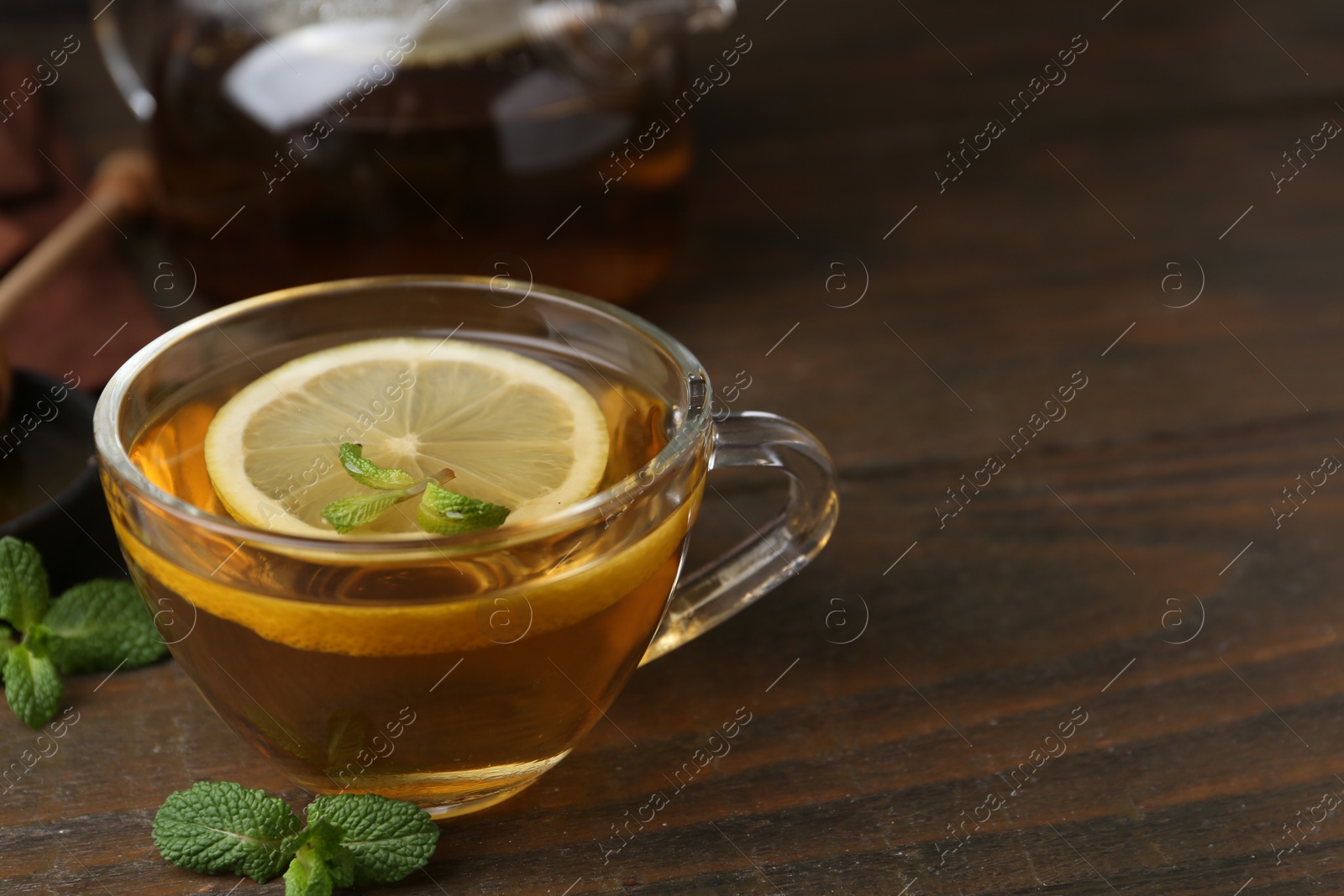 Photo of Tasty mint tea in cup, lemon and fresh leaves on wooden table, closeup. Space for text