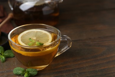 Photo of Tasty mint tea in cup, lemon and fresh leaves on wooden table, closeup. Space for text