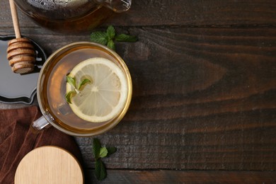 Photo of Tasty mint tea in cup, lemon and fresh leaves on wooden table, flat lay. Space for text