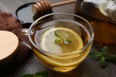 Photo of Tasty mint tea in cup, lemon and fresh leaves on wooden table, closeup