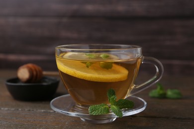 Photo of Tasty mint tea in cup, lemon and fresh leaves on wooden table, closeup