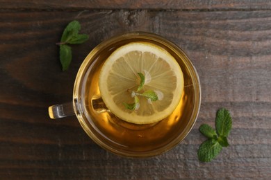 Photo of Tasty mint tea in cup, lemon and fresh leaves on wooden table, flat lay