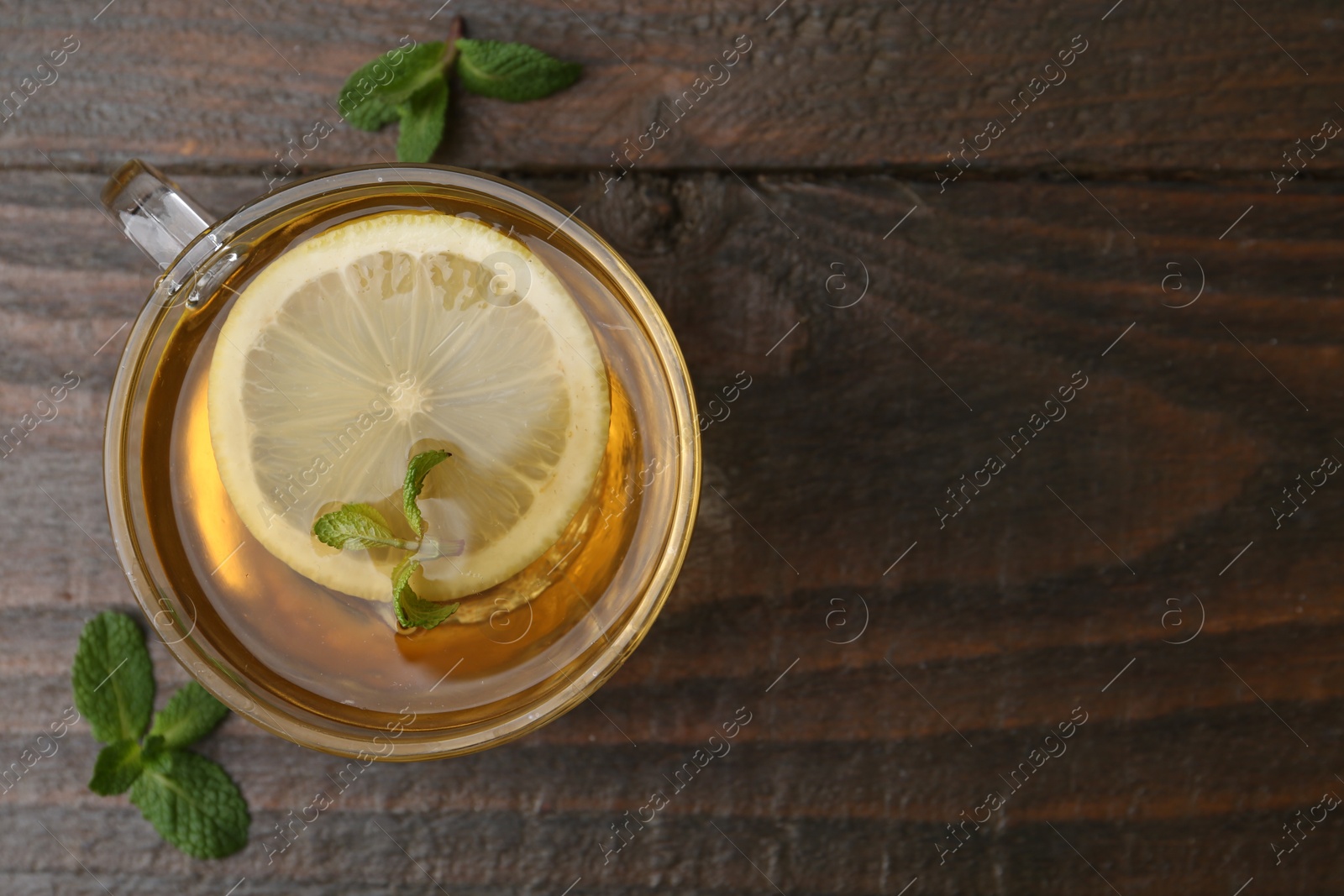 Photo of Tasty mint tea in cup, lemon and fresh leaves on wooden table, flat lay. Space for text