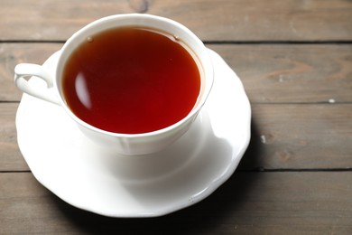 Photo of Refreshing black tea in cup on wooden table, closeup