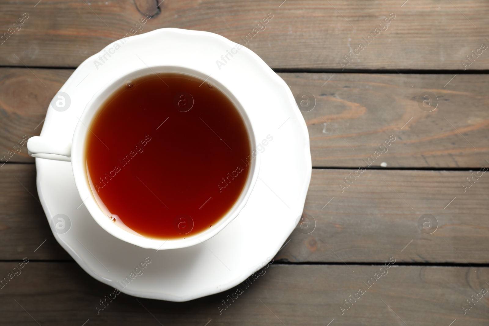 Photo of Refreshing black tea in cup on wooden table, top view. Space for text