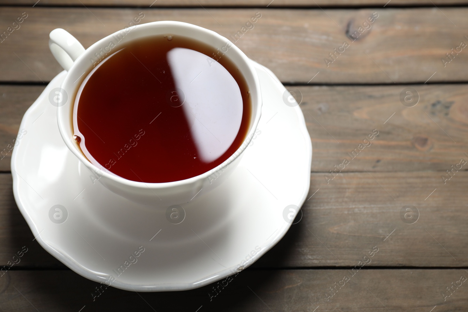 Photo of Refreshing black tea in cup on wooden table, closeup. Space for text