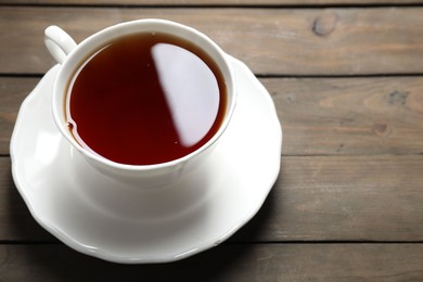 Photo of Refreshing black tea in cup on wooden table, closeup. Space for text