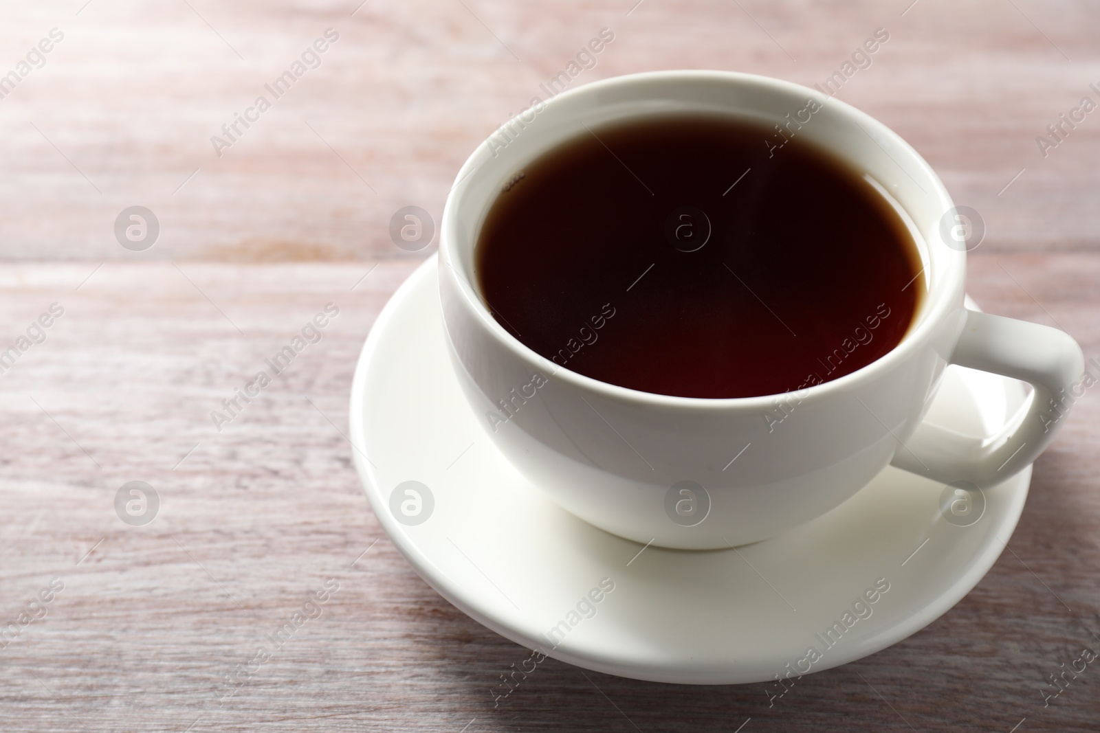 Photo of Refreshing black tea in cup on light wooden table, closeup