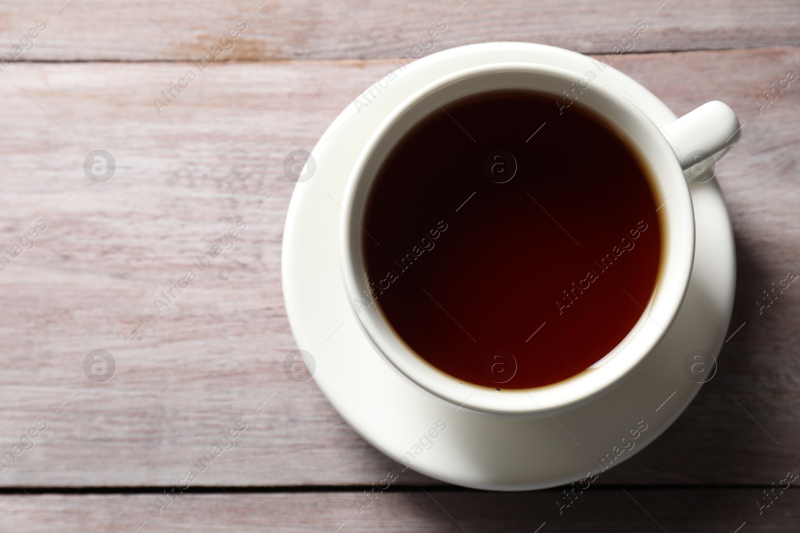 Photo of Refreshing black tea in cup on light wooden table, top view. Space for text