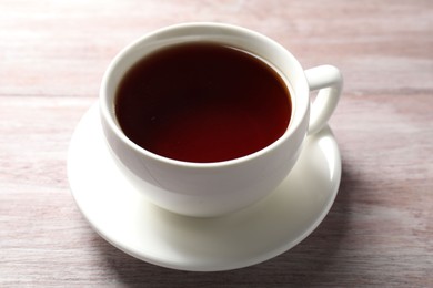 Photo of Refreshing black tea in cup on light wooden table, closeup