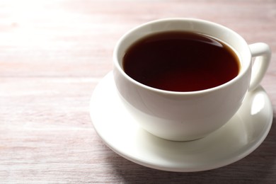 Photo of Refreshing black tea in cup on light wooden table, closeup. Space for text