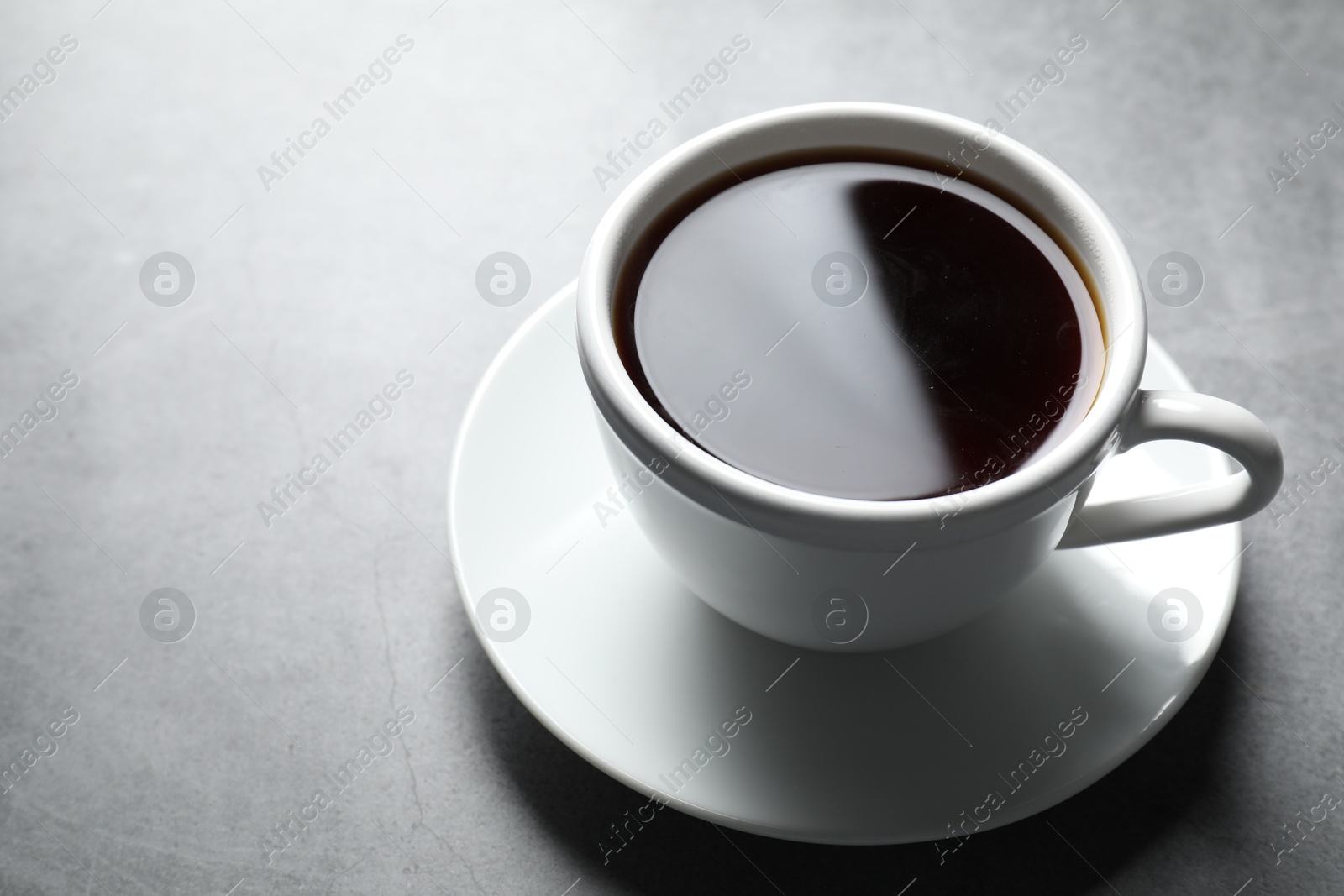 Photo of Refreshing black tea in cup on grey table, closeup. Space for text