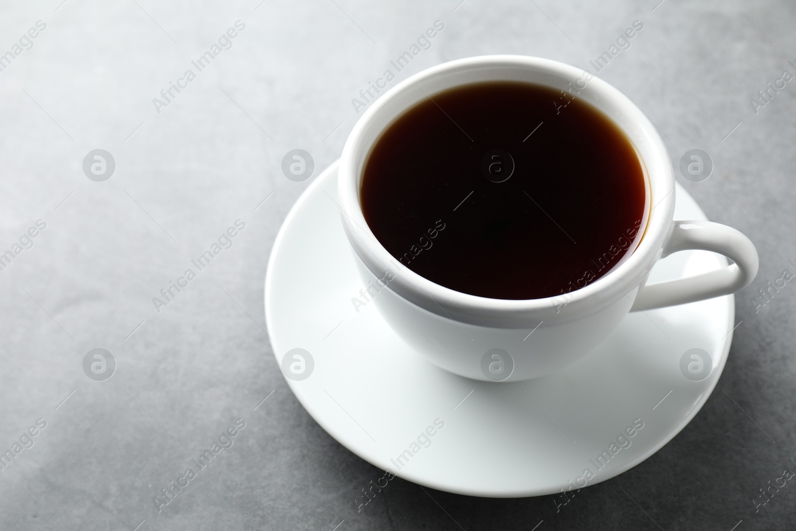 Photo of Refreshing black tea in cup on grey table, closeup. Space for text