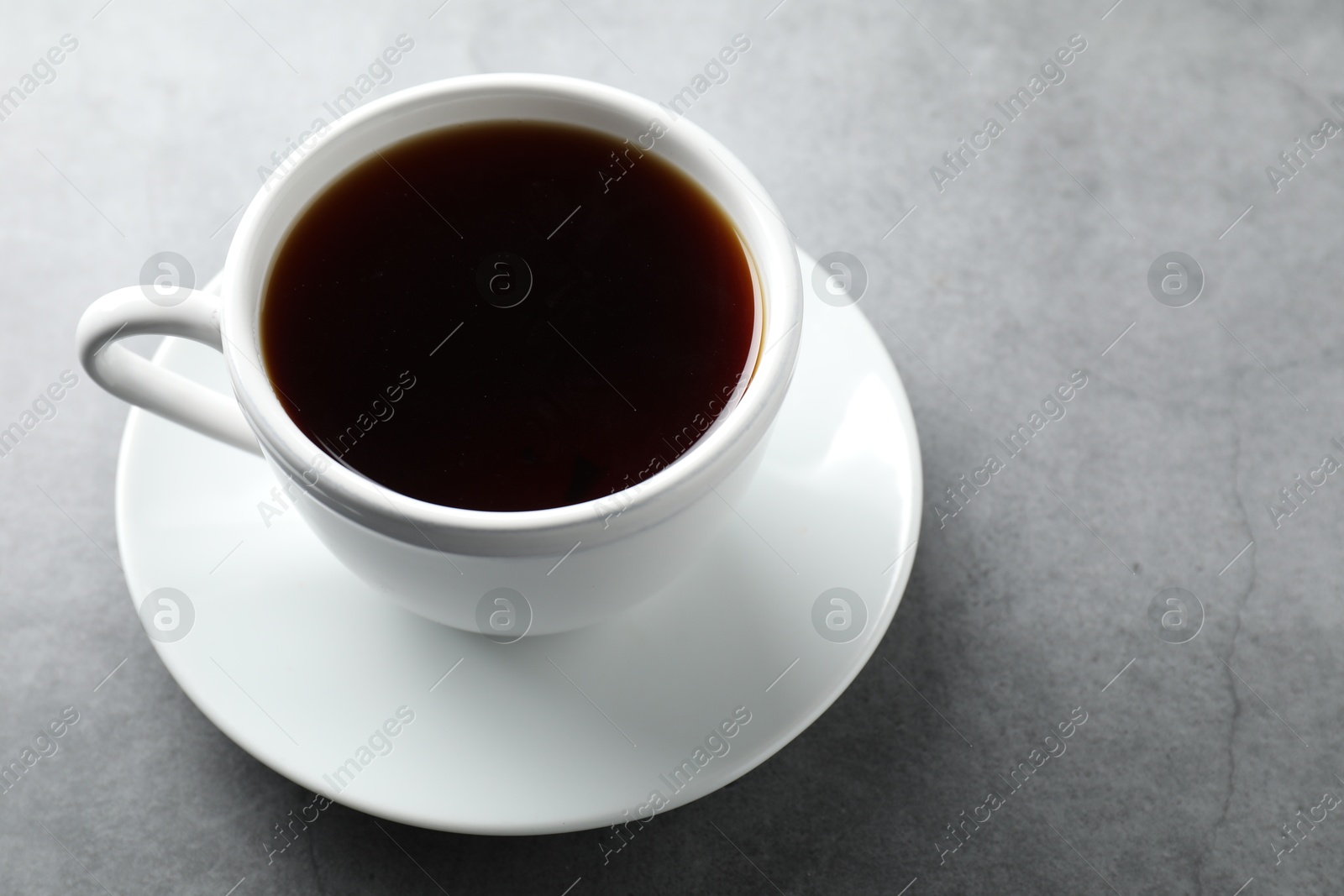 Photo of Refreshing black tea in cup on grey table, closeup. Space for text