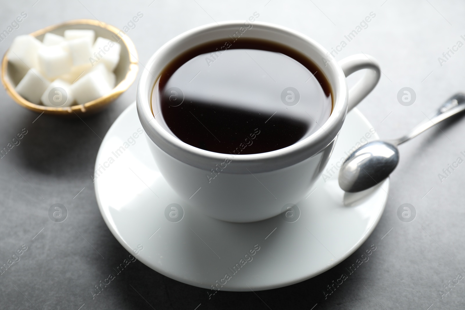 Photo of Refreshing black tea in cup, spoon and sugar cubes on grey table, closeup