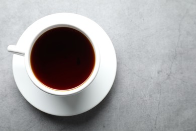 Photo of Refreshing black tea in cup on grey textured table, top view. Space for text