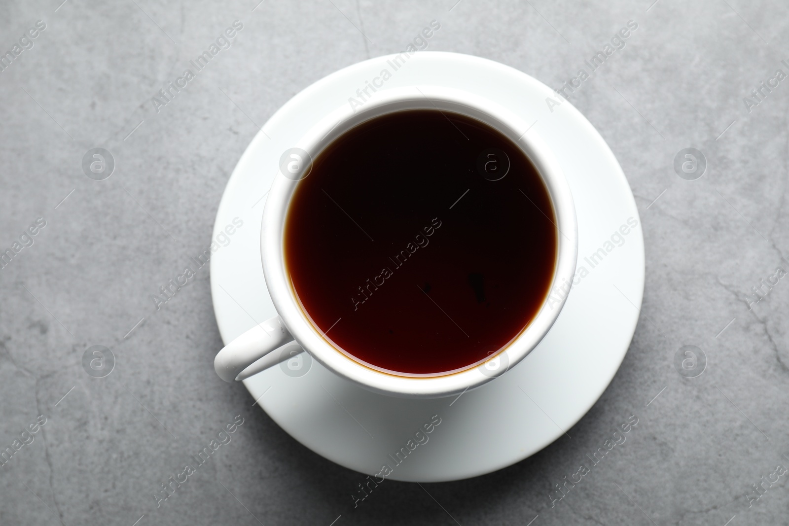 Photo of Refreshing black tea in cup on grey textured table, top view